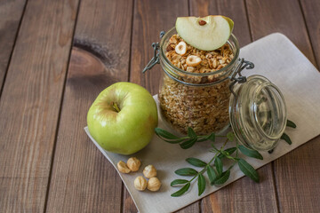 A glass jar with homemade muesli with nuts and a green apple. Healthy breakfast.