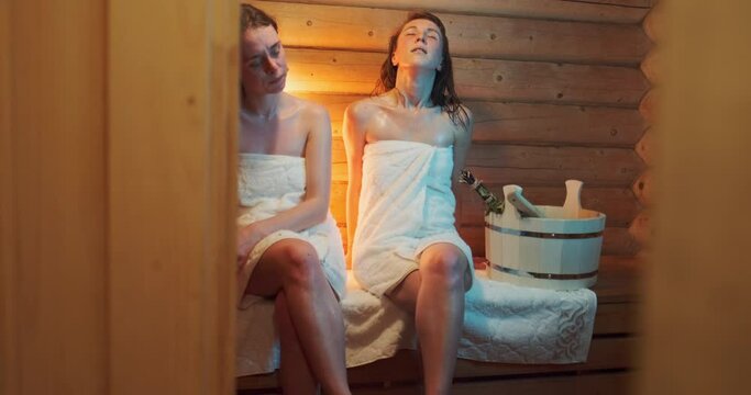 Women In Sauna. Two Young Women Relax In A Hot Wooden Sauna