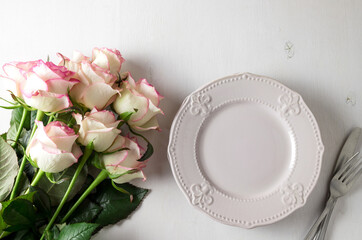 Plate on white background and pink roses. Top view