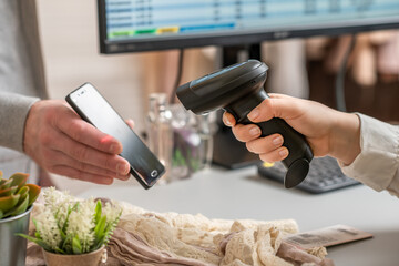 Woman cashier scanning qr code from buyer phone using barcode scanner. Man buying a gift in a...