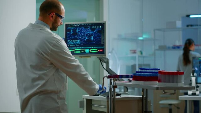 Scientist worried about virus evolution analysing DNA scan image standing in equipped laboratory typing at computer. Stuff examining vaccine development using high tech researching treatment