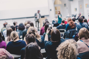 Obraz premium Male speaker giving presentation in lecture hall at university workshop. Audience in conference hall. Rear view of unrecognized participant in audience. Scientific conference event.