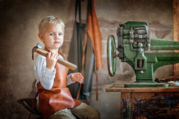 blond little boy sitting at the bench and holding a hammer. children and work
