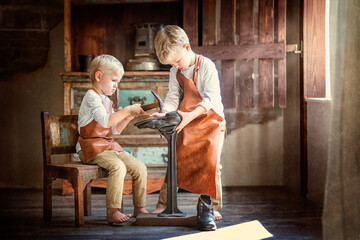 two little brothers in white shirts, aprons and trousers with bare feet playing shoemakers.