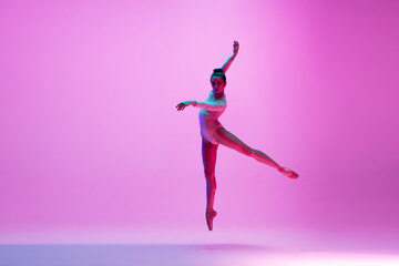 Fototapeta na wymiar High above. Young and graceful ballet dancer on pink studio background in neon light. Art, motion, action, flexibility, inspiration concept. Flexible caucasian ballet dancer, moves in glow.