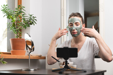 Beautiful white women making an online course of facial skin care and treatment with a green clay mask.