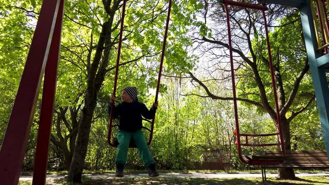 Little boy having fun on outdoor playground. Swinging on swing. 
