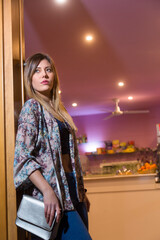 Bellissima ragazza bruna vestita con abiti casual posa con espressione seria all'ingresso di un bar