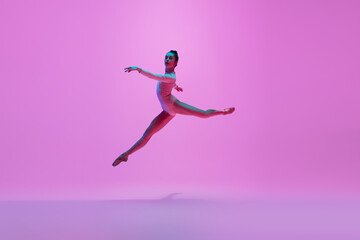 Fototapeta na wymiar Beautiful. Young and graceful ballet dancer on pink studio background in neon light. Art, motion, action, flexibility, inspiration concept. Flexible caucasian ballet dancer, moves in glow.