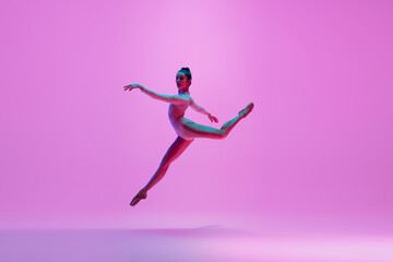 Fototapeta na wymiar Inspiration. Young and graceful ballet dancer on pink studio background in neon light. Art, motion, action, flexibility, inspiration concept. Flexible caucasian ballet dancer, moves in glow.