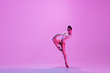 Naklejka na ściany i meble Urban style. Young and graceful ballet dancer on pink studio background in neon light. Art, motion, action, flexibility, inspiration concept. Flexible caucasian ballet dancer, moves in glow.