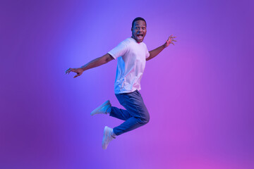 Happy Excited Black Man Jumping In Neon Light Over Purple Background, Full-Length