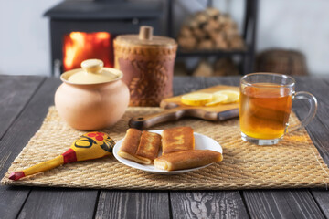 Pancakes with filling and tea with lemon on a wooden table against the background of a burning fireplace and wood-burning stove, still life with food in rustic styles