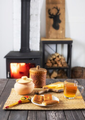 Pancakes with filling and tea with lemon on a wooden table against the background of a burning fireplace and wood-burning stove, still life with food in rustic styles .in cozy atmosphere at home