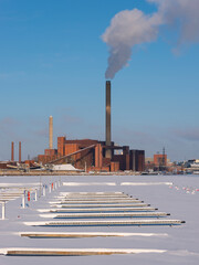 A wintery scene of an urban power plant with a frozen lake in the foreground.