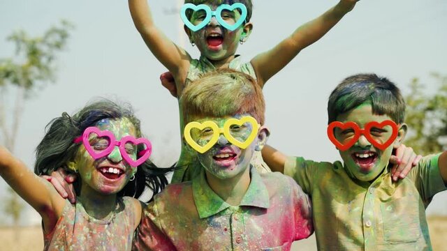 Group of Cheerful kids with fun spectacles Shouting at camera after playing with colourful holi powder during festival celebration