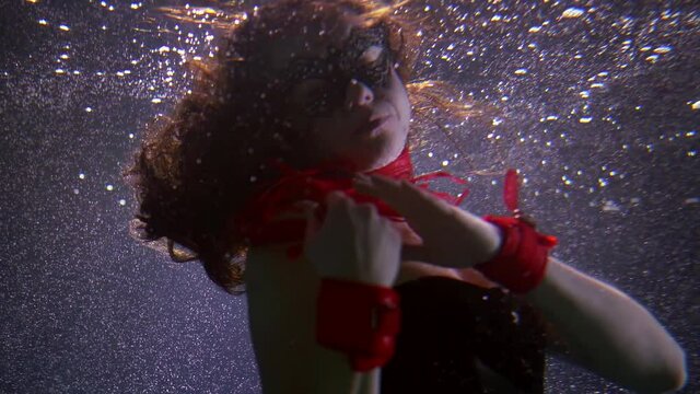 sexual woman is wearing mysterious mask and corset is swimming underwater, stroking her body by knout