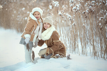 Fototapeta na wymiar Family walk in winter park Two girls girl wearing white mittens and a white hat playing with snow standing in the snow cuddling. Christmas