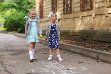 Two girls with pigtails and bows in blue dresses play in the courtyard in classics. The concept of a fun children's summer vacation