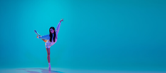 Young and graceful ballet dancer isolated on blue studio background in neon light. Art, motion, action, flexibility, inspiration concept. Flexible caucasian ballet dancer, moves in glow. Flyer