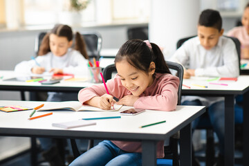 Portrait of small asian girl sitting at desk in classroom