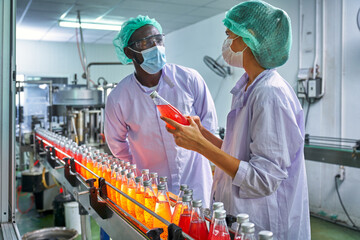 African and Caucasian Lab Specialist are discussing with quality of red juice in product line of...