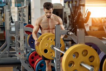 Fototapeta na wymiar Strong athletic young man bodybuilder fitness model put weights on barbell on the bench in gym.