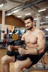Fototapeta na wymiar Muscular athletic young man bodybuilder fitness model focusing on exercise with dumbbell in the gym.