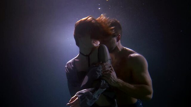 lovers underwater, passionate embrace man and woman in dark deepness, slow motion
