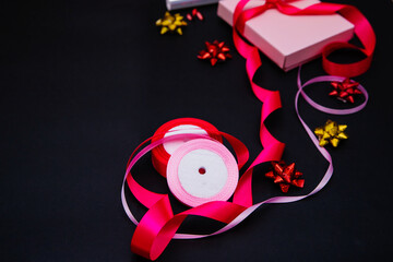 On a black background, there is a pink gift box. The box is tied with a satin ribbon.Gift wrapping.