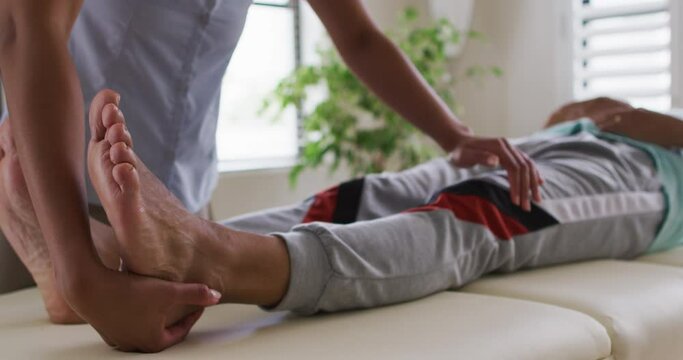 Mixed race female physiotherapist helping senior man stretching his legs