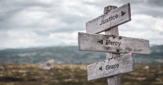 justice mercy grace text engraved on wooden signpost outdoors in nature. Panorama format.