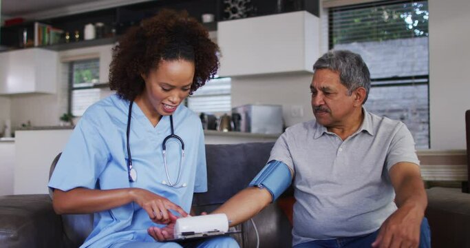 Senior mixed race man with female doctor home visiting taking blood pressure