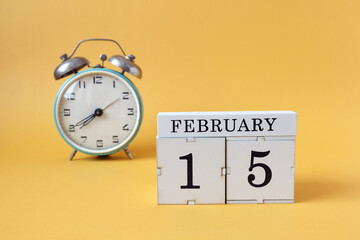 Calendar for February 15: cubes with the number 15 and the name of the month, alarm clock on a yellow background