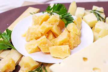 Variety of parmesan and maasdam pieces cheese in the kitchen on light background.