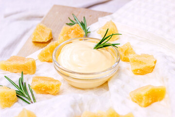 Fresh homemade creamy cheese sauce in a glass bowl with rosemary and parmesan pieces on light background.