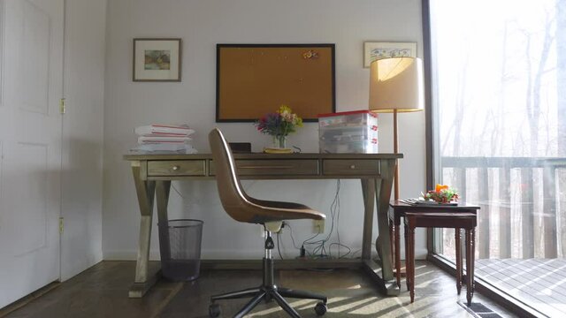 Plymouth, IN USA - January 14th 2021: an empty office by the window with the afternoon sunlight coming in the apartment. isolated chair with lamp and wood furniture 