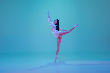 Art. Young and graceful ballet dancer isolated on blue studio background in neon light. Art, motion, action, flexibility, inspiration concept. Flexible caucasian ballet dancer, moves in glow.