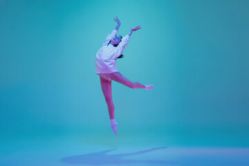 Fototapeta na wymiar Flying high. Young and graceful ballet dancer isolated on blue studio background in neon light. Art, motion, action, flexibility, inspiration concept. Flexible caucasian ballet dancer, moves in glow.