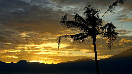 Sonnenaufgang in tropischer Landschaft beim Vulkan Mt. Gede mit gelbem Schein vor dunklen Wolken
