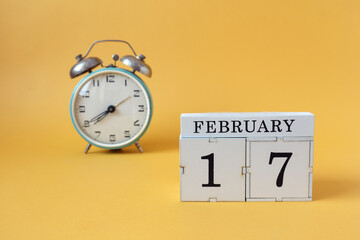 Calendar for February 17: cubes with the number 17 and the name of the month, alarm clock on a yellow background