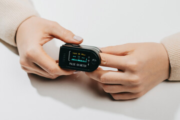 Woman put on pulse oximeter on finger, check blood oxygen saturation. Monitoring heart rate at home during pandemic coronavirus covid-19