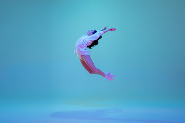 Fototapeta na wymiar Flying high. Young and graceful ballet dancer isolated on blue studio background in neon light. Art, motion, action, flexibility, inspiration concept. Flexible caucasian ballet dancer, moves in glow.