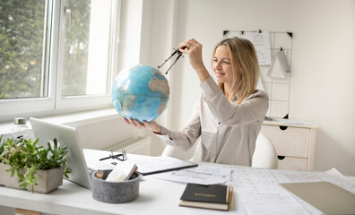 young, beautiful female architect is sitting in her office and is holding a globe and is dreaming...