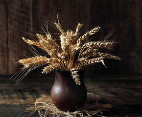 Still life with a bouquet of wheat ears in a clay jug on a wooden table.