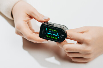 Woman put on pulse oximeter on finger, check blood oxygen saturation. Monitoring heart rate at home during pandemic coronavirus covid-19