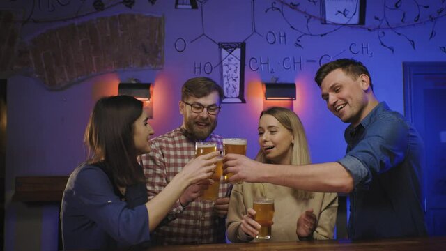 Friends in pub drink beer on bar counter clink glasses. Happy people enjoy weekend