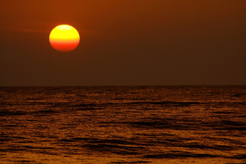 View on tropical sunset with big round sun over ocean horizon, dark shimmering water - Sri Lanka