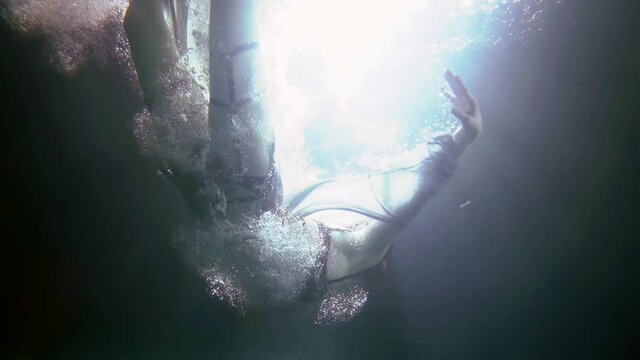 young graceful woman is plunging underwater, falling inside ocean, sea or pool, subaquatic slow motion shot