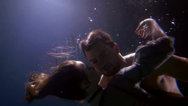 young heterosexual pair is floating underwater, romantic man and woman are hugging inside water
